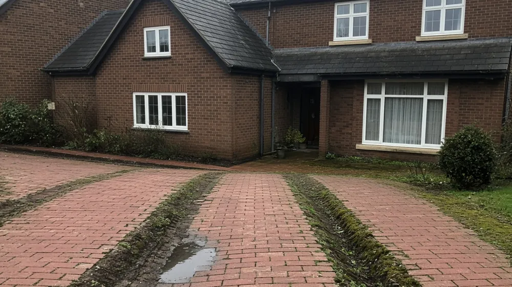 Older block paving sunk in the wheel tracks with weeds growing in the joints